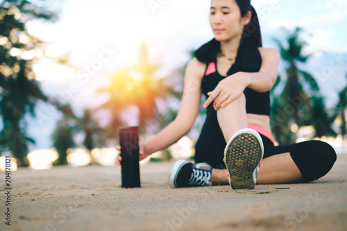 Fototapeta Naklejka Na Ścianę i Meble -  Asia beautiful woman in sport ware sitting on the beach and drinking water after exercise. 
