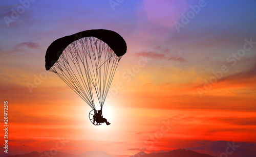 silhouette paraglider flying with paramotor on sunset