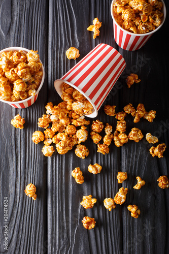 Boxes with wweet caramel popcorn, black table, Snack for cinema closeup. Vertical top view