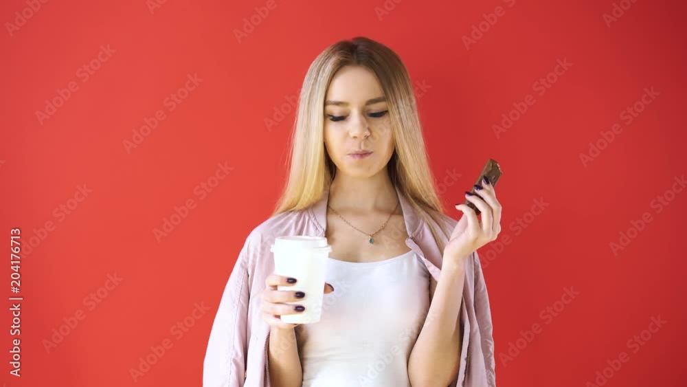 Girl on a red background, bites chocolate and drinks coffee Girl on a red background, bites chocolate and drinks coffee