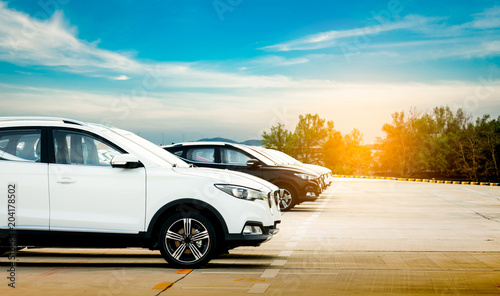 Luxury white and black new suv car parked on concrete parking area at factory with blue sky and clouds. Car stock for sale. Car factory parking lot. Automotive Industry concept. Car dealership.