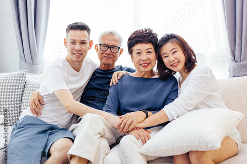 Asian family with adult children and senior parents relaxing on a sofa at home together