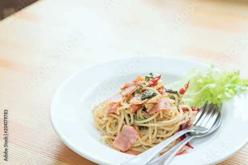 Spaghetti pasta with ham and a spoon on the table. Natural light tableware.