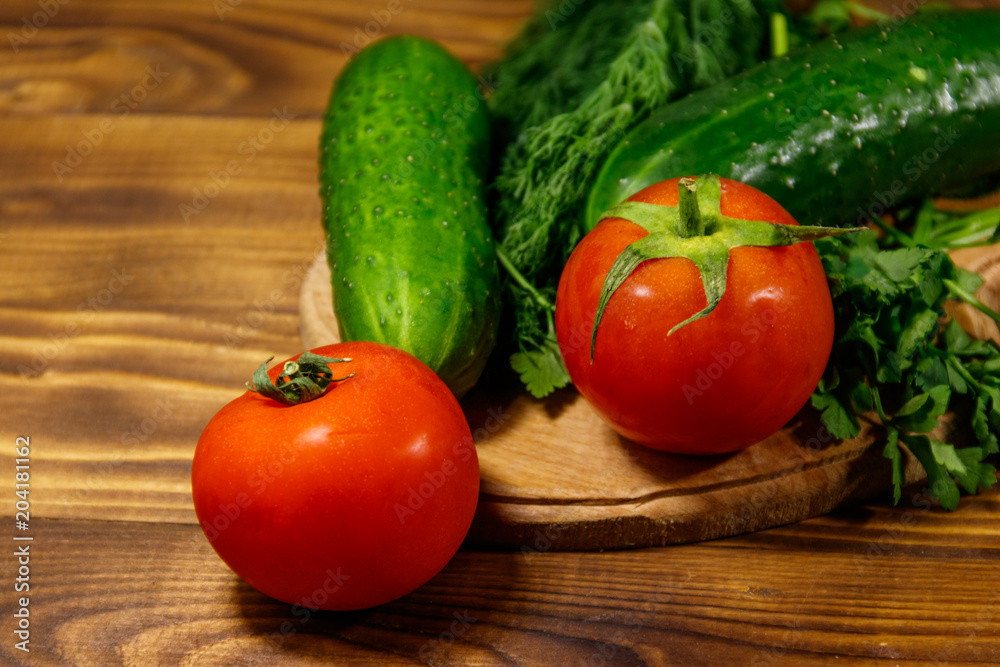 Fresh tomatoes, cucumbers, parsley and dill on cutting board on wooden table Fresh tomatoes, cucumbers, parsley and dill on cutting board on wooden table
