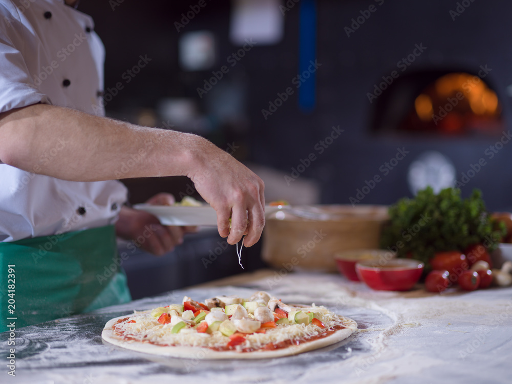 chef putting fresh vegetables on pizza dough