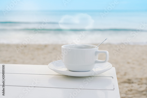 white hot coffee cup with heart shaped smoke on wooden desk near beach in morning, pastel tone, valentine concept
