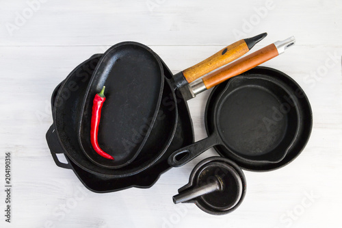 Cast iron cookware, pans, pots on white wooden table.