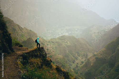 Hiker with backpack on the mountain top. Rocky terrain of a incredible panorama view of high mountain ranges and deep ravines around. Santo Antao Cape Verde
