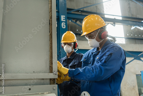 Two blue-collar workers wearing protective equipment while insulating an industrial pressure vessel
