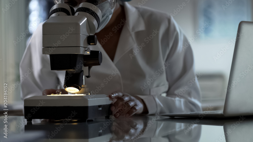 Female researcher looking at test sample under microscope, working in clinic Female researcher looking at test sample under microscope, working in clinic