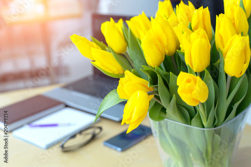 Large beautiful bouquet of yellow tulips on a desk in the office. Congratulations on the holiday or birthday. Flowers as a gift.