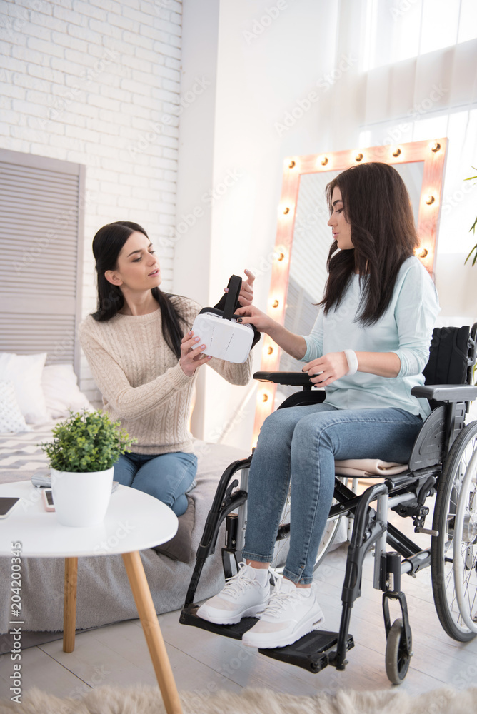 Innovative technology. Musing friend and crippled woman holding VR headset and looking down Innovative technology. Musing friend and crippled woman holding VR headset and looking down