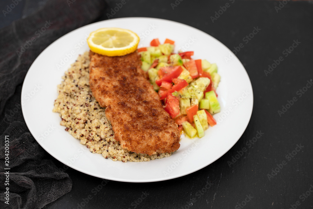 fried fish with salad, qiuinoa and lemon on white plate