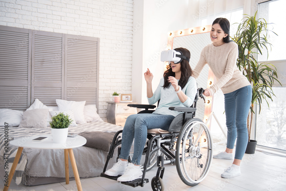 Virtual universe. Gay friend standing while immobile woman wearing VR glasses Virtual universe. Gay friend standing while immobile woman wearing VR glasses