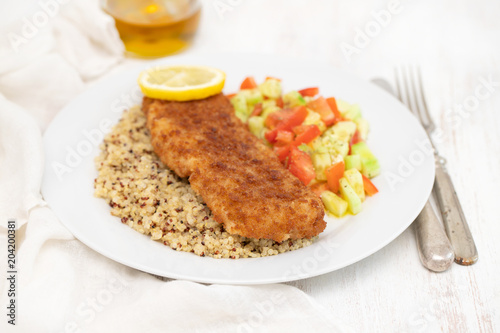 fried fish with salad, qiuinoa and lemon on white plate