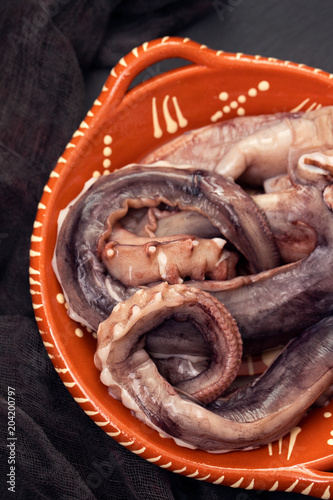 raw octopus on brown ceramic dish on black background