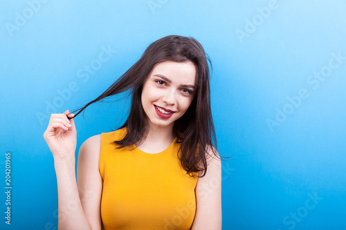 Smilng woman playing with her hair on blue background