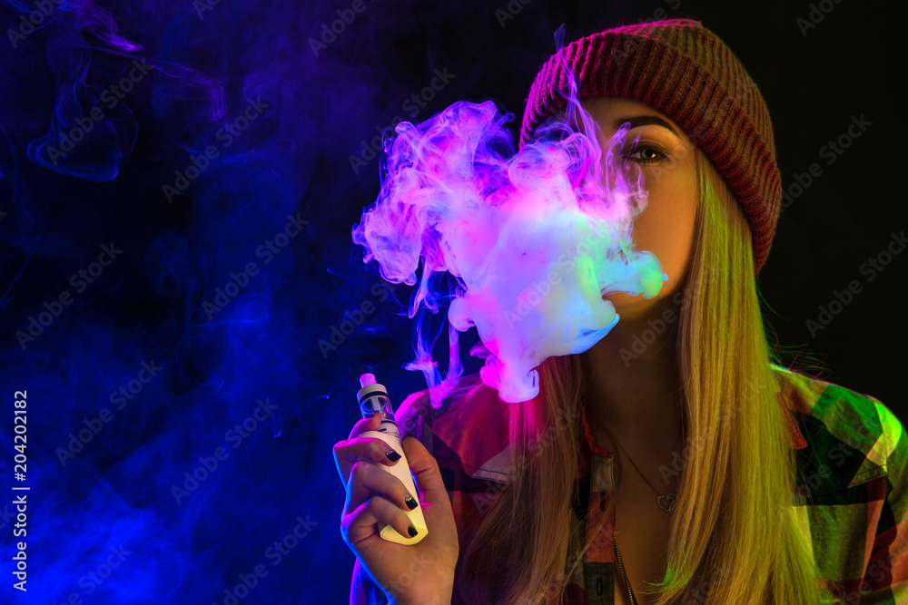 Vaping girl. Young hipster woman vape e-cig on studio on black background. Hip-hop style. Close up.