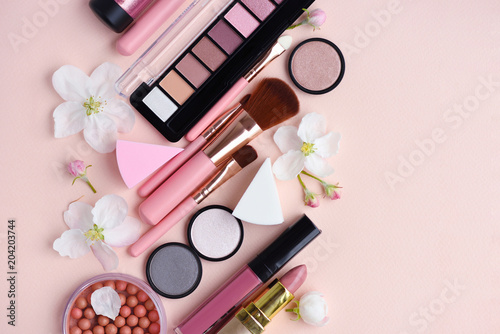 Makeup brush and decorative cosmetics with apple blossom on pink background. Top view