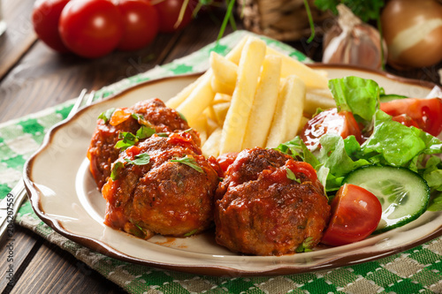 Roasted meatballs in tomato sauce with french fries and salad