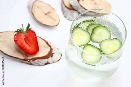 Detox flavored water with cucumber on white background with red strawberry and wood decoration. Healthy food concept.  Refreshing summer homemade cocktail. Copy space