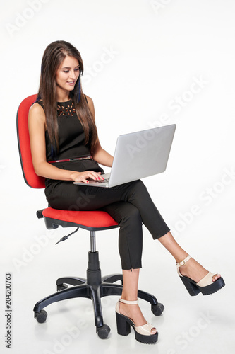 Business woman sitting on office chair working with laptop, full length portrait