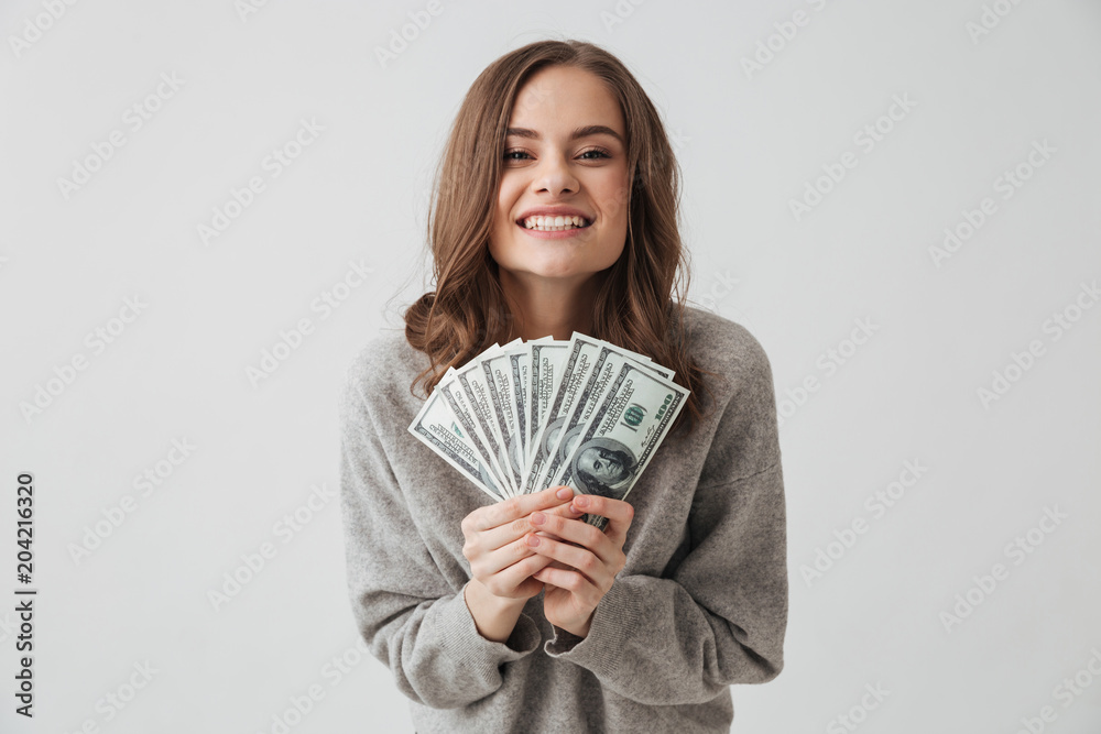 Cheerful brunette woman in sweater holding money and rejoices Cheerful brunette woman in sweater holding money and rejoices