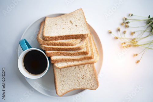 The blue ceramic coffee cup with black coffee put beside sliced bread,on white table,blurry light around.