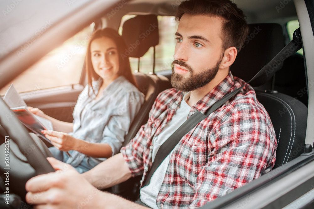 Careful and nice guy is driving car and looking straight forward. He is paying all of his attention to the road. Girl is sitting besides him. She is holding map and looking at young man with smile. Careful and nice guy is driving car and looking straight forward. He is paying all of his attention to the road. Girl is sitting besides him. She is holding map and looking at young man with smile.