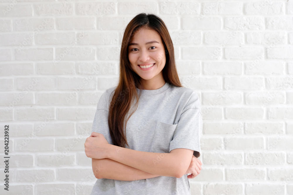 Portrait of young asian woman standing and smiling over white brick wall background