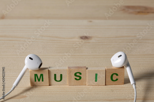 earphones on wooden block with the word music and; a large space for your text photo