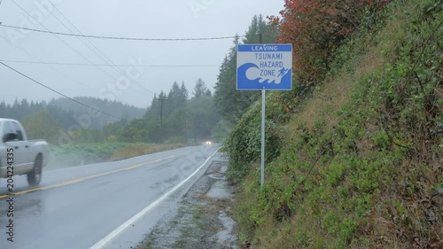 car passes a tsunami sign on the side of the road in a rain storm.