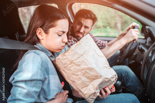 A picture of sick girl holding a bag and trying to vomit into it. She feels bad. Girl is holding her hand on stomach. Guy is looking at her with sight full of disgution. photo