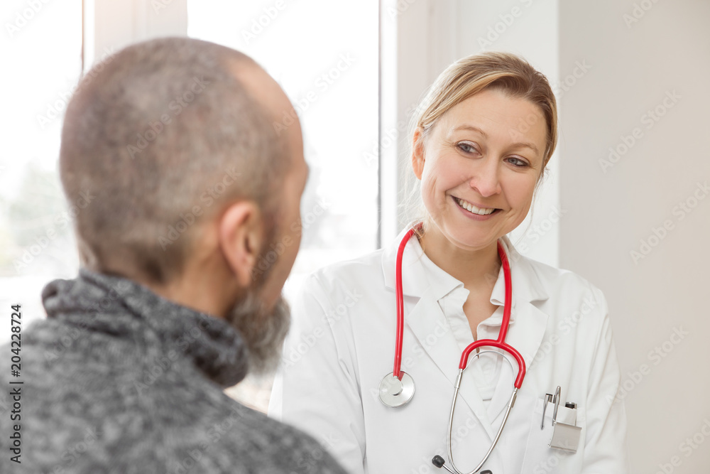 Ärztin lächelt Patient an, Behandlungsraum von Praxis mit Textfreiraum Ärztin lächelt Patient an, Behandlungsraum von Praxis mit Textfreiraum