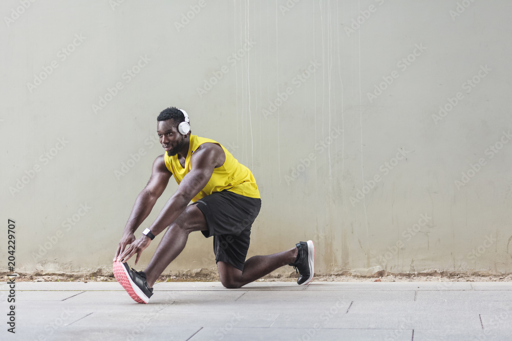 Afro runner in yellow sportswear stretching before doing morning workout
