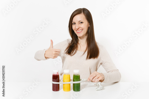 Young woman at table with green, red, yellow detox smoothies in bottles, measure tape isolated on white background. Proper nutrition, vegetarian drink, healthy lifestyle, dieting concept. Copy space.