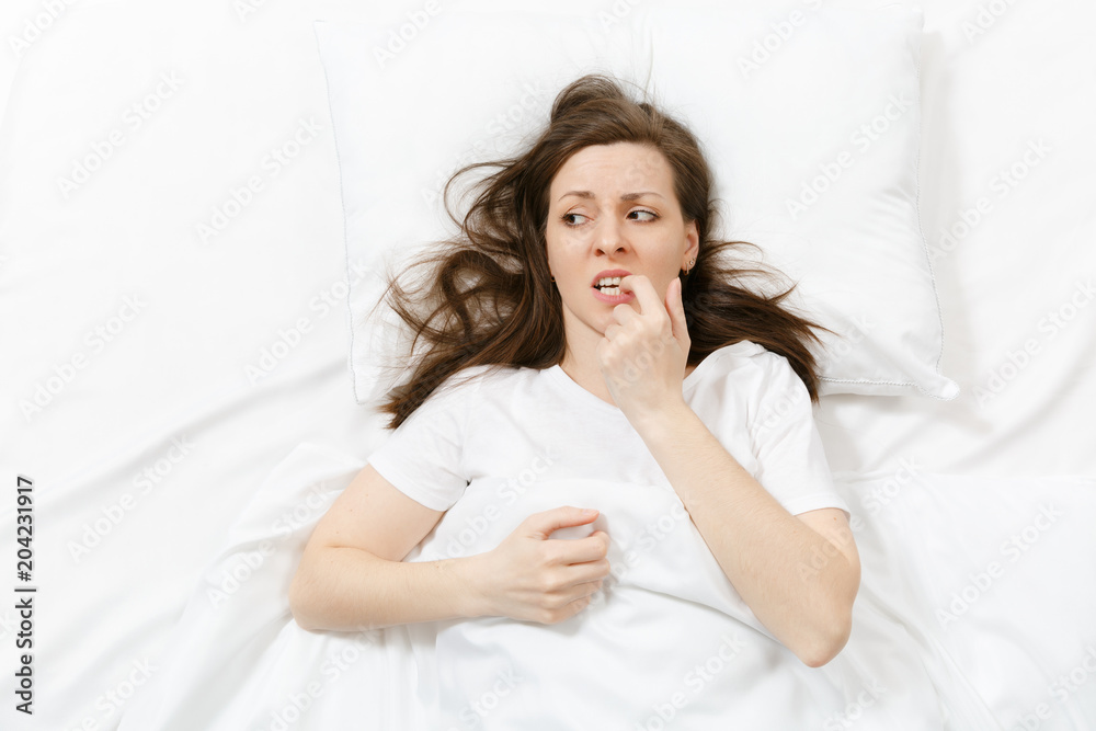 Top view of tired stressed crying young woman lying in bed with white sheet, pillow, blanket. Pensive frustrated sad upset female spending time in room. Rest, relax, bad mood concept. Copy space. Top view of tired stressed crying young woman lying in bed with white sheet, pillow, blanket. Pensive frustrated sad upset female spending time in room. Rest, relax, bad mood concept. Copy space.