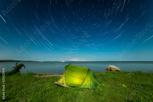Camping on the shore of lake under star trail sky