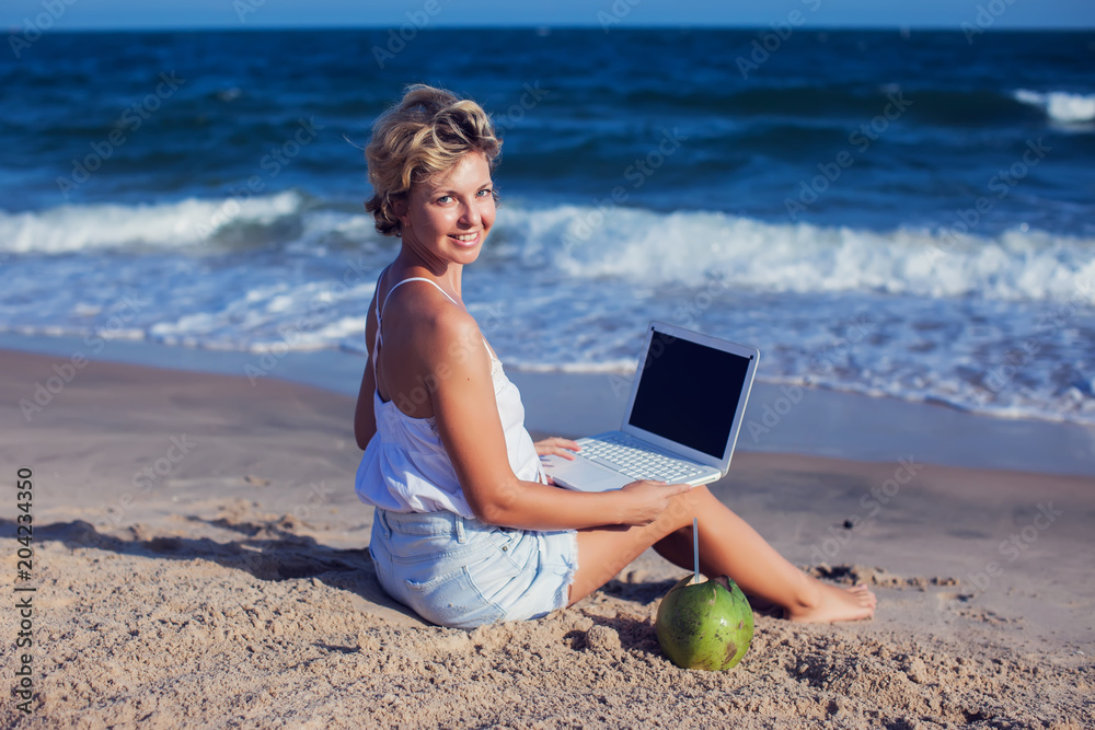 Beautiful casual woman with a laptop on the beach with the sea in the background