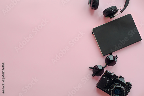 stylish black photo camera,headphones, sunglasses and notebook on trendy pink background, flat lay. space for text. modern hipster travel and wanderlust image. summer vacation
