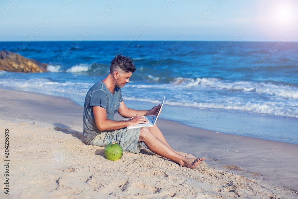 Young man sitting on beach with laptop