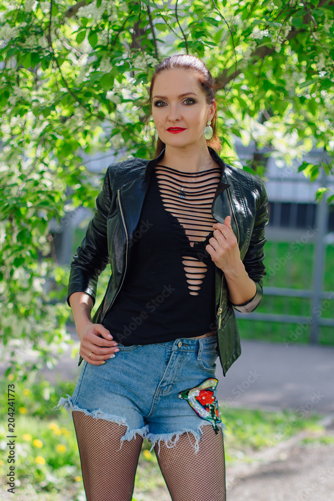 Fototapeta premium Charming woman dressed in a leather jacket near bird-cherry tree