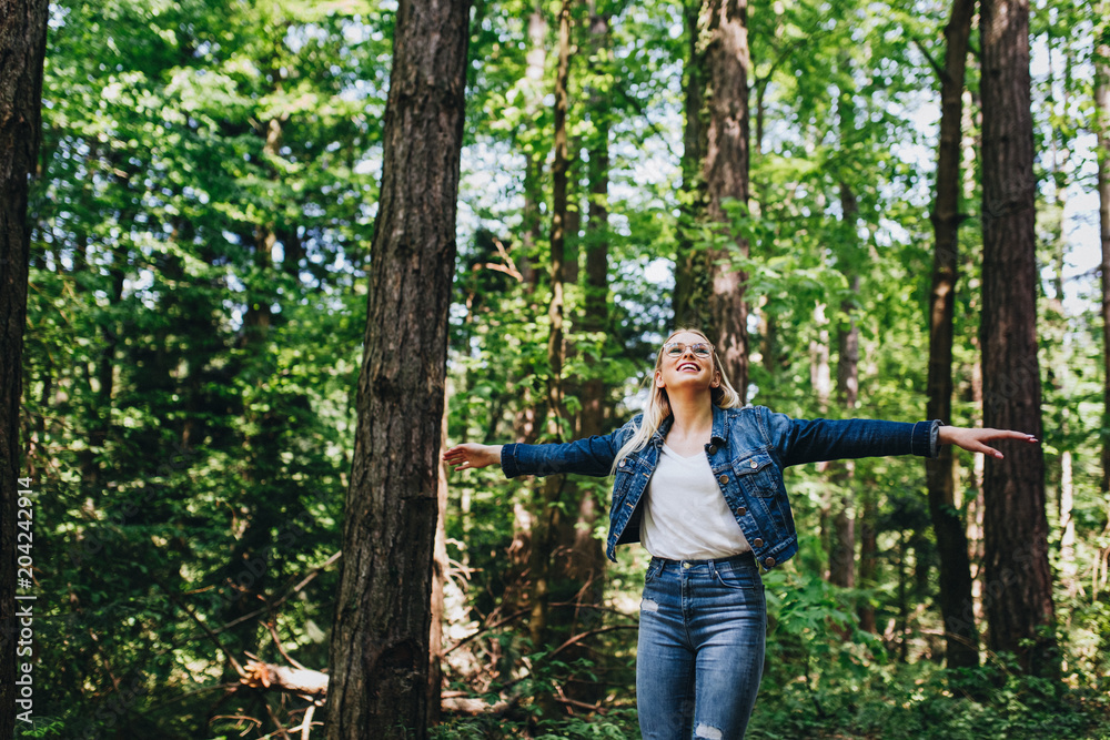 Young blond woman enjoying the nature, outstretched arms while enjoying the fresh air in green forest Young blond woman enjoying the nature, outstretched arms while enjoying the fresh air in green forest