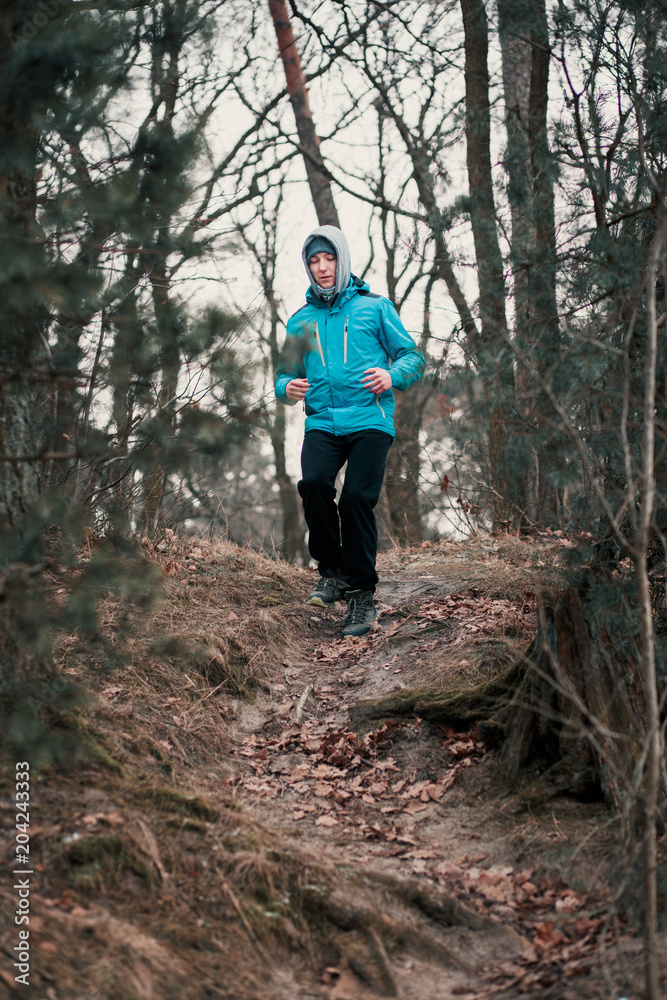 Young man running outdoors during workout in a forest among leafless trees on cold freeze autumn day