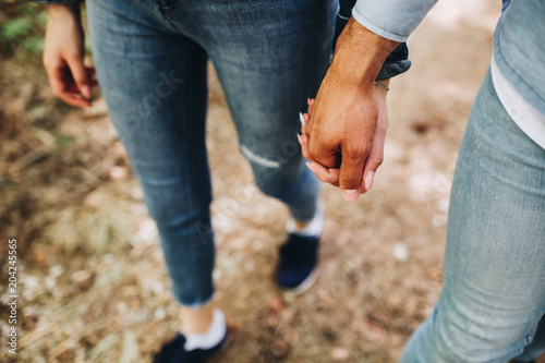 Close up on young couple walking, hand in hand, through forest