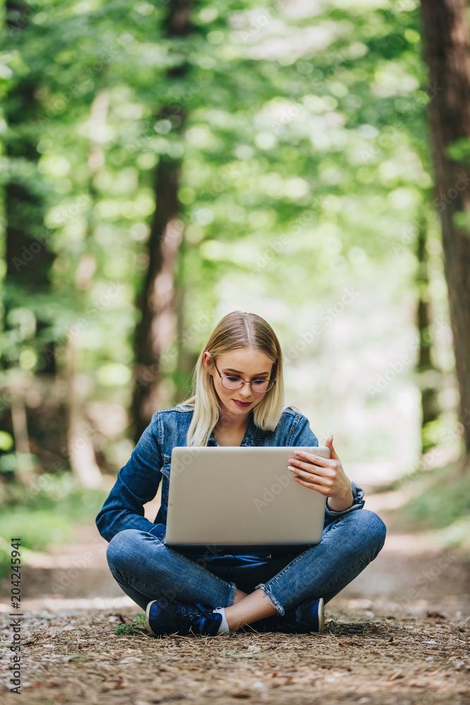 Young cheerful woman using laptop while sitting in forest Young cheerful woman using laptop while sitting in forest