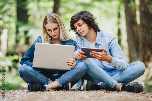 Young couple using laptop and tablet while sitting in forest