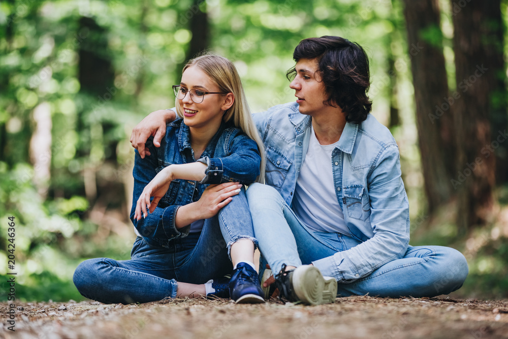 Romantic young couple sitting together in forest and enjoying sunny day together