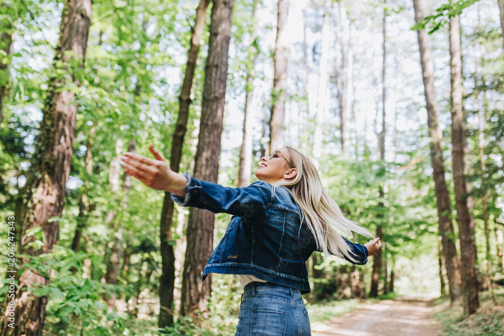 Young blond woman enjoying the nature, outstretched arms while enjoying the fresh air in green forest Young blond woman enjoying the nature, outstretched arms while enjoying the fresh air in green forest