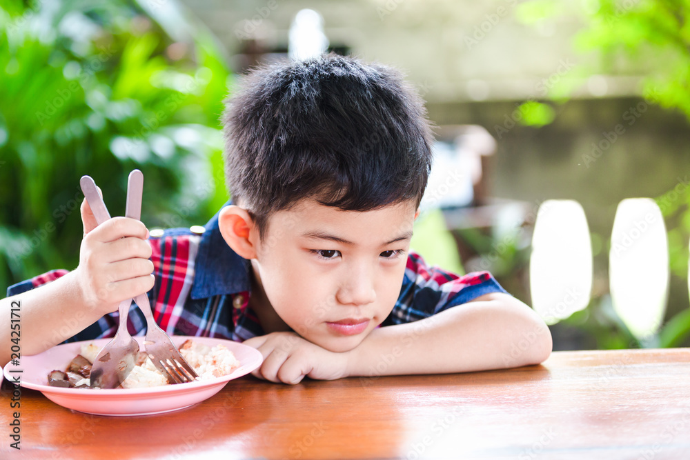 Asian little boy boring eating with rice food on the wooden table Asian little boy boring eating with rice food on the wooden table